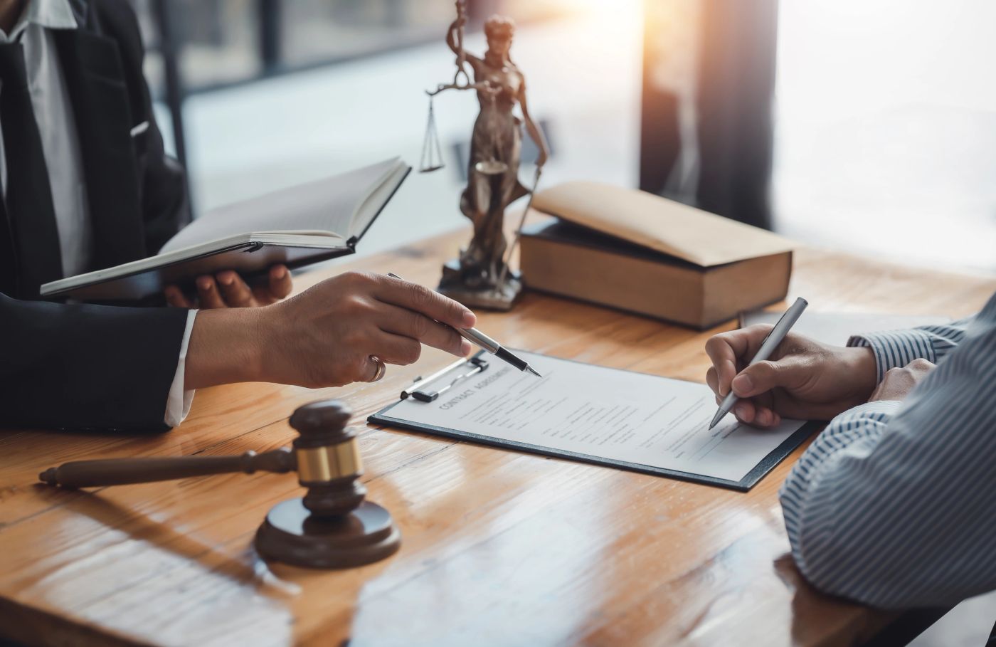 An attorney and client reviewing and signing a contract at a desk.