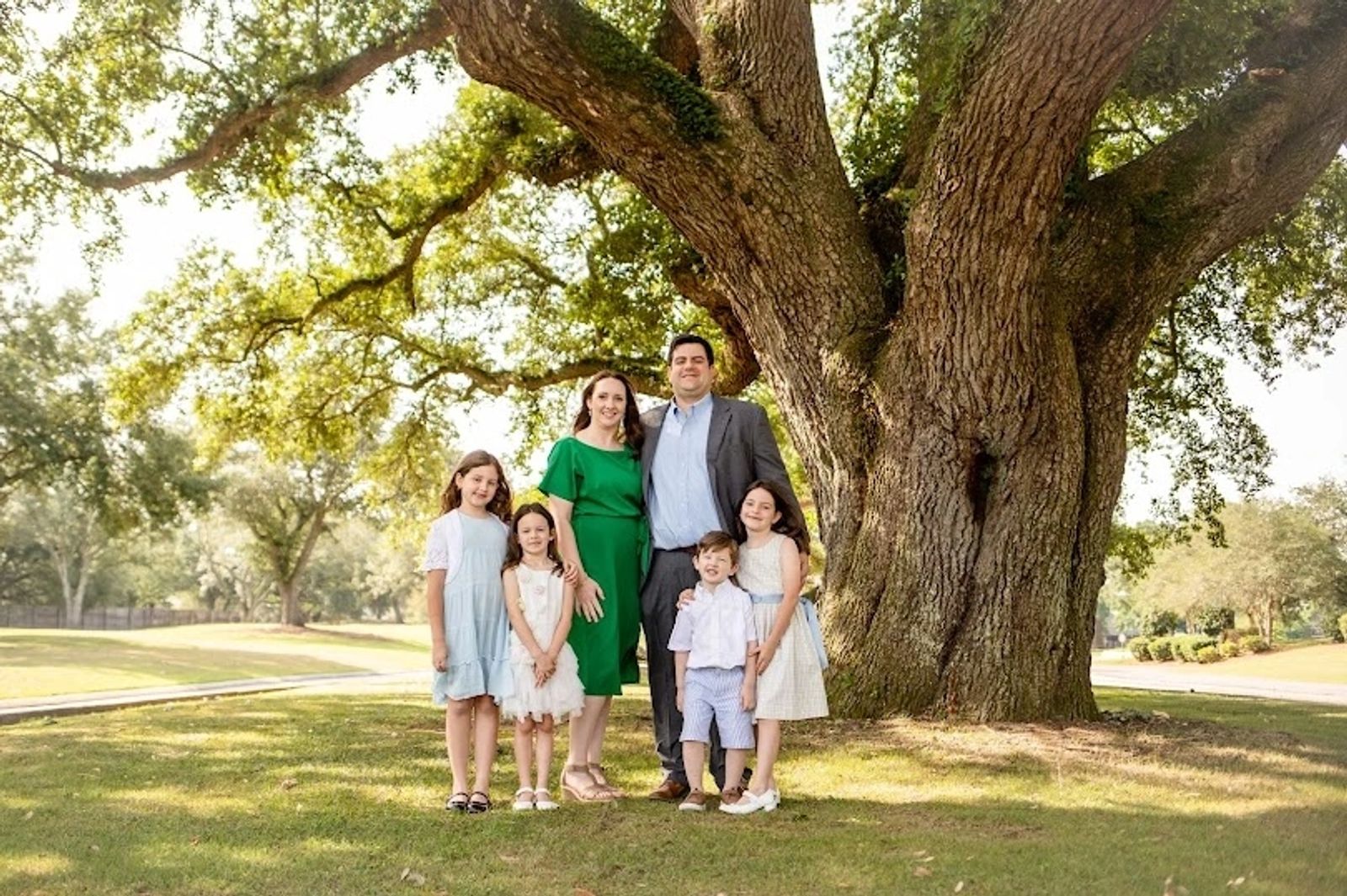 John Tilly’s family of six posing together outdoors beneath a large oak tree.